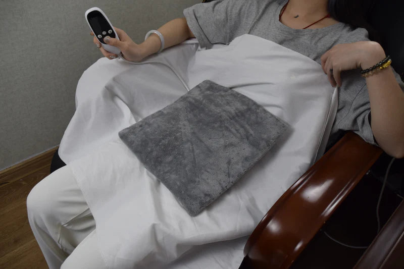 Person holding a gray heating pad on a white blanket